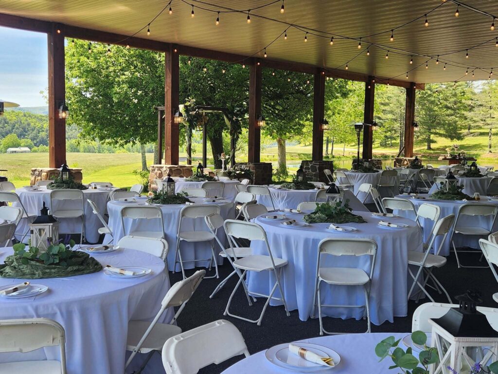 Round tables set under the waterside pavilion with string lights and open views to the fields