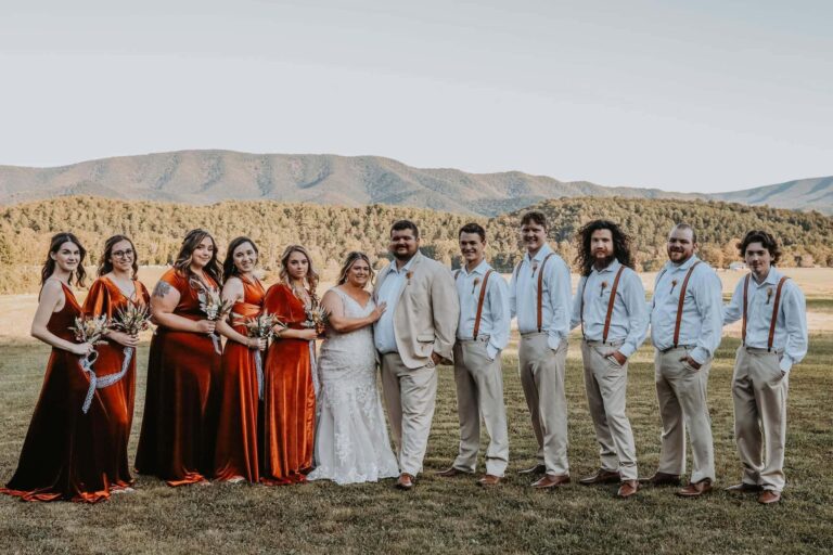 Full wedding party lined up in an autumn field with the mountain ridge behind them